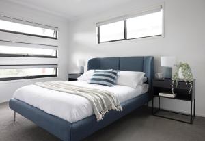 a blue bed in a bedroom with two windows at Seagrass in Vincentia