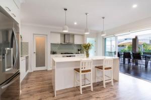 a kitchen with a white counter and chairs in it at Sea Change in Shellharbour