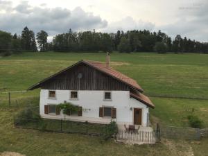 een wit huis met een bruin dak in een veld bij la ferme de la gaby in Le Noirmont