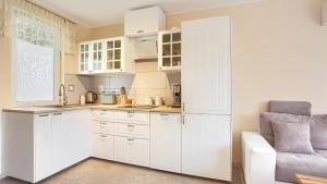 a white kitchen with white cabinets and a chair at Apartamenty Sun & Snow Rumiankowa in Rewal