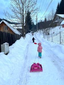 Ein Kind zieht einen Schlitten im Schnee in der Unterkunft Casuta noastra din Predeal in Predeal