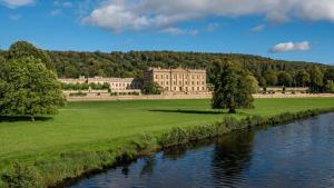 a large building in a field next to a river at Hawkfield in Baslow