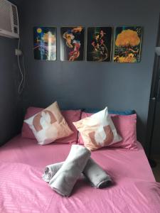 a bed with pink sheets and pillows with pictures on the wall at Simple & Cozy 1 Bedroom US Embassy, Roxas Blvd, Ermita, Manila in Manila