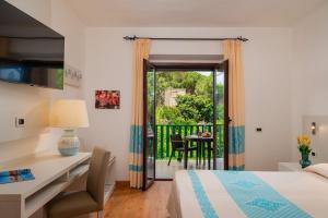 a bedroom with a bed and a desk and a balcony at Hotel Dei Pini in Alghero