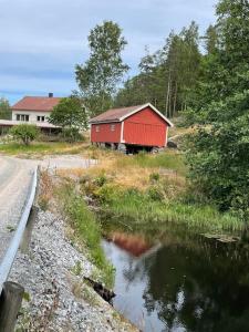 a red barn next to a road and a river at Trivelig nyoppusset hus ved femsjøen. in Halden
