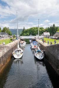 three boats are docked in a canal with people walking around at Loch Ness Gate House in Fort Augustus