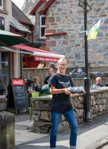 Człowiek stojący na chodniku trzymający tacę z jedzeniem w obiekcie Loch Ness Gate House w mieście Fort Augustus