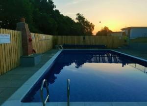 a swimming pool in front of a fence with the sunset at Greenways Valley Holiday Park in Great Torrington