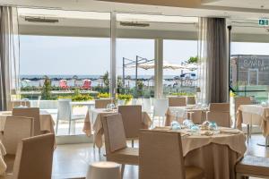 un restaurante con mesas y sillas blancas y ventanas grandes en Hotel Savini, en Bellaria-Igea Marina