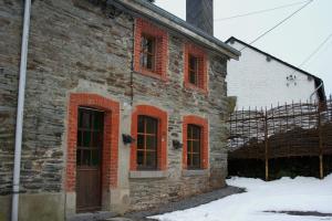 an old brick building with red windows in the snow at La ferme Claudlisse in Vielsalm