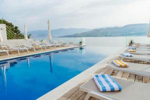 a swimming pool with lounge chairs and the water at Hotel Plaza in Pag