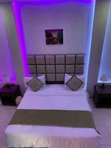 a bedroom with a large white bed with purple lights at منتجع الجزيرة الخضراء in Al Hada