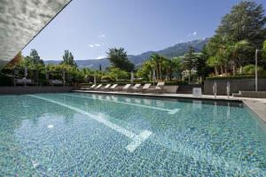 a swimming pool with chairs and mountains in the background at Feldhof DolceVita Resort in Naturno