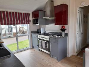 a kitchen with a stove and red cabinets and a window at Pebble Lodge in Tydd Saint Giles