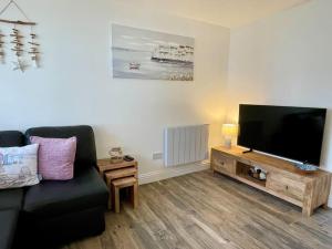 a living room with a black couch and a flat screen tv at Little Greenway Holiday Bungalow in Galmpton-on-the-Dart