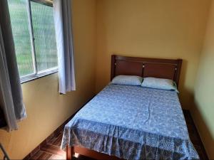 sypialnia z łóżkiem z niebieską kołdrą i oknem w obiekcie Teresópolis Hostel w mieście Teresópolis