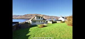 a house on a grassy hill next to a body of water at Ormasaig, Self Catering, One Mile to Town & close to Ben Nevis in Fort William