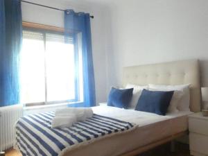 a bed with blue and white pillows and a window at Apartamento Marisol Confort in Aroeira