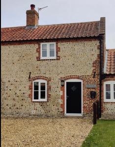 a brick house with a black door and windows at Alicias Cottage, Bacton in Norwich