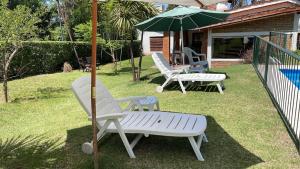 two white chairs and an umbrella on a yard at Casa con jardín, pileta, asador, y vistas al lago en Embalsina in Villa del Dique