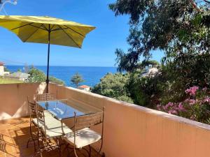 een tafel en stoelen op een balkon met een parasol bij Bas de villa T3 sur santa maria di lota in Santa-Maria-di-Lota