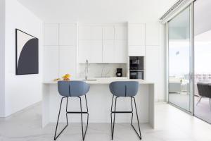 a kitchen with white cabinets and blue bar stools at Crystal I Luxury Apartments by EnjoyaHome in Santiago del Teide