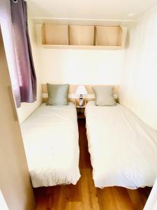 duas camas num pequeno quarto com lençóis brancos em Évasion océanique : Mobil-home dans un camping 4* à 50m de l'océan em La Bétaudière