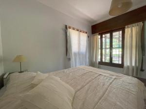 1 cama blanca en un dormitorio con ventana en La Casita de Córdoba en Capilla del Monte