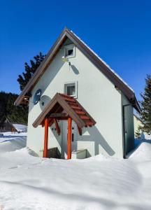 a small white building with a wooden roof in the snow at Holiday Home Ljuban in Risovac