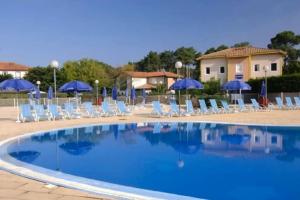 a swimming pool with chairs and blue umbrellas at Charmante petite maison in Soustons