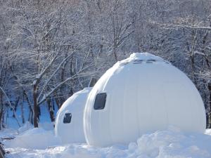 deux maisons igloo couvertes de neige devant des arbres dans l'établissement Redoor Sapporo, à Sapporo