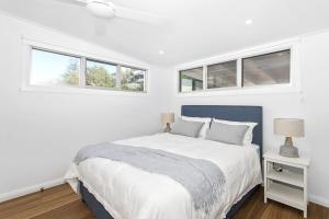 a white bedroom with a bed and two windows at Pas Beach House Apartment 2 in Mollymook