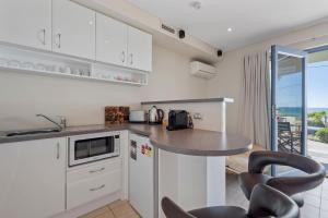 a kitchen with white cabinets and a counter with chairs at Aqua Shores Studio in Mollymook