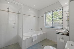 a white bathroom with a tub and a sink at Aqua Shores Penthouse in Mollymook +18 photos