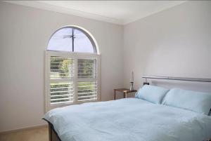 a bedroom with a white bed and an arched window at Kokomo on Village in Ulladulla +6 photos