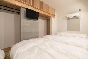 七尾市にあるSocial Guest House neltokoの白いベッド3台、壁にテレビが備わる客室です。