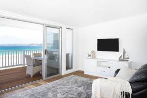 a living room with a couch and a tv and a balcony at Pas Beach House Apartment 1 in Mollymook