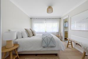 a white bedroom with a bed and a lamp at Coast House Mollymook in Mollymook