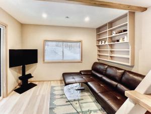 a living room with a leather couch and a television at Piccolo House in Hakuba