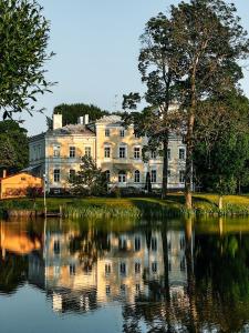 une grande maison blanche avec sa réflexion dans l'eau dans l'établissement Igates pils, à Myza Igate