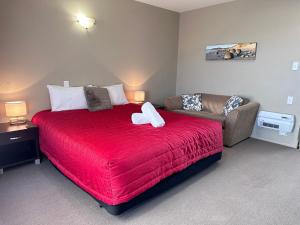 um quarto com uma cama vermelha e um sofá em Heritage Court Motor Lodge Oamaru em Oamaru