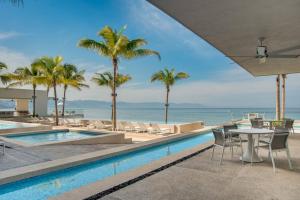 una piscina con sillas, una mesa y palmeras en Harbor 3008 Amazing beach front condo by Moikkarentals, en Puerto Vallarta