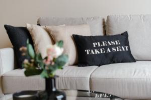 a couch with a pillow that says please take a seat at Premium Apartment - Allocated Parking - Great Location in Plymouth