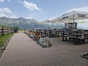 a patio with benches and umbrellas with mountains in the background at Almgasthaus Glocknerblick in Großkirchheim