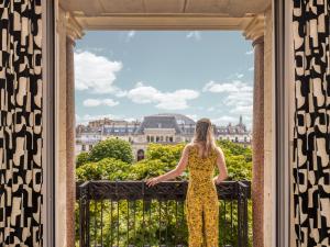 Una donna con un vestito giallo che guarda fuori da una finestra a Versailles di Solly Hôtel Paris a Parigi