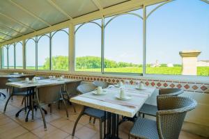 a dining room with tables and chairs and windows at Hôtel de Margaux in Margaux