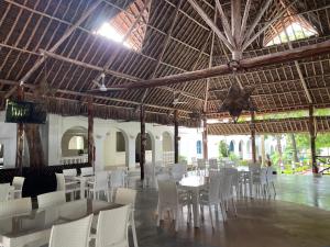 a restaurant with white tables and chairs and a large ceiling at Maasai Resort in Mombasa