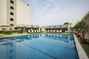 Ramada by Wyndham Bahrain في المنامة: وجود مسبح في الفندق مع الكراسي والمظلات