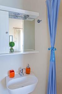 Tourlos Beachfront House in Mykonos في تورلوس: حوض الحمام مع مرآة وستارة زرقاء