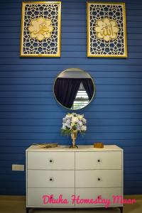a dresser with a mirror and a vase of flowers on it at Dhuha Homestay Muar in Muar